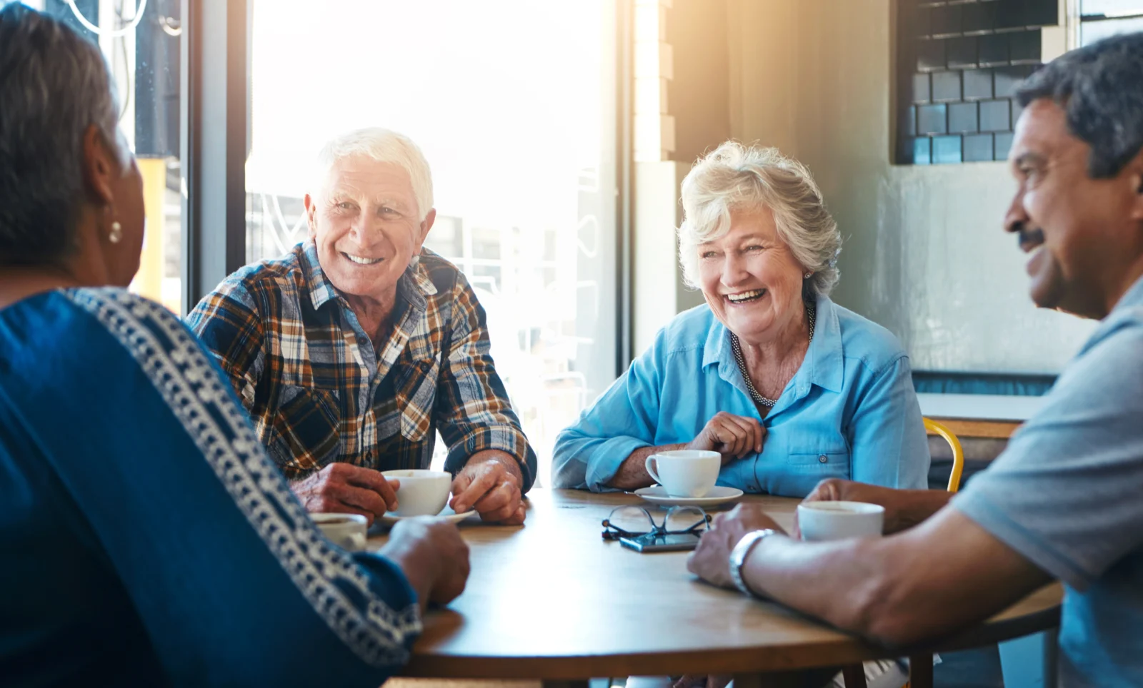 A group of older people sitting around a table with hot drinks